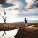 Water crisis concept, Hopeless and lonely farmer sit on cracked earth near drying water.