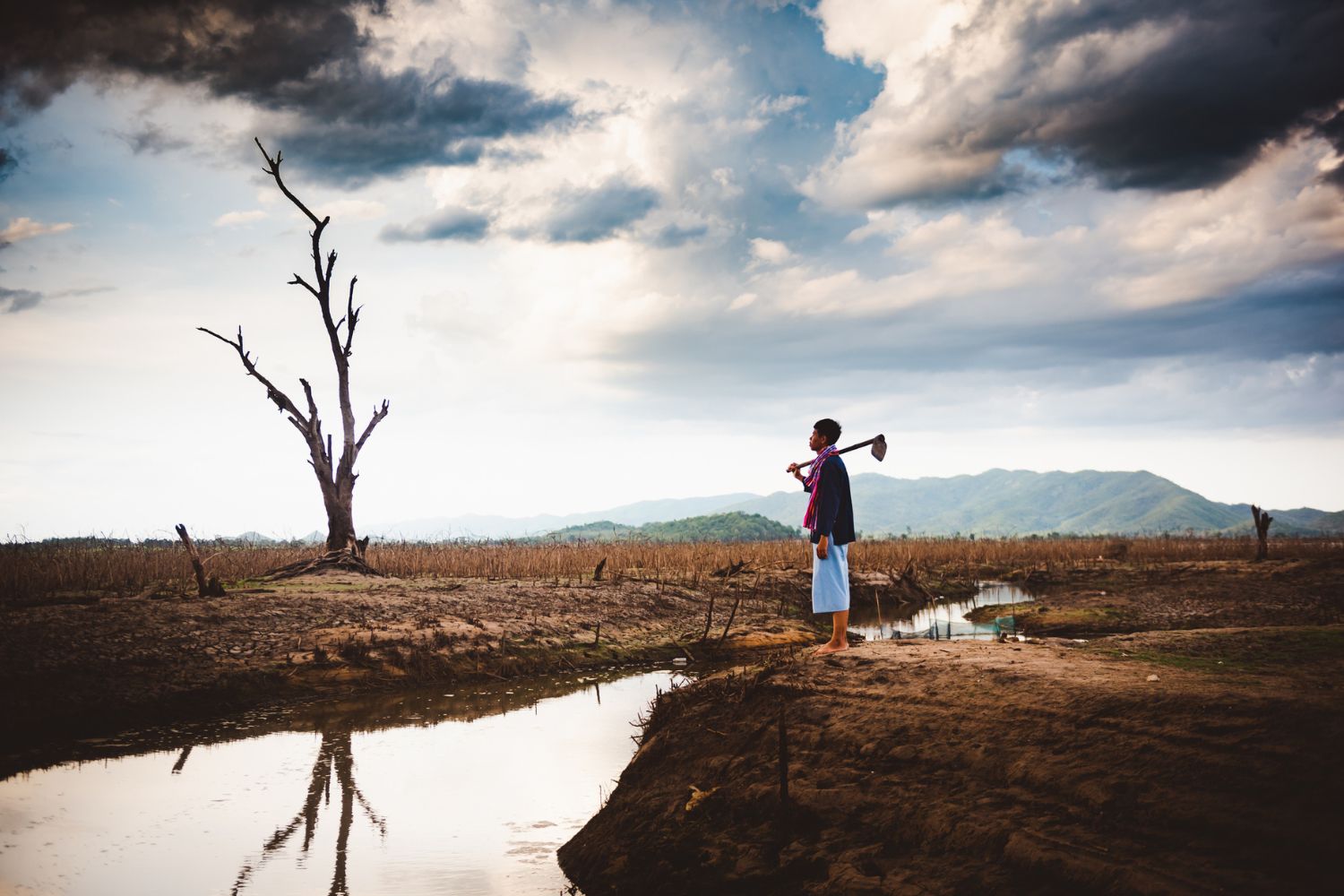 Water crisis concept, Hopeless and lonely farmer sit on cracked earth near drying water.