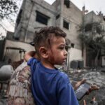 Gaza Strip after Israeli retaliatory rockets. A little boy, wounded in the conflict stand in front of ruins.