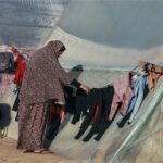 A woman hangs up clothes at a camp for displaced Palestinians in Rafah in the southern Gaza Strip on December 16, 2023, amid continuing battles between Israel and the militant group Hamas. (Photo by MOHAMMED ABED / AFP)