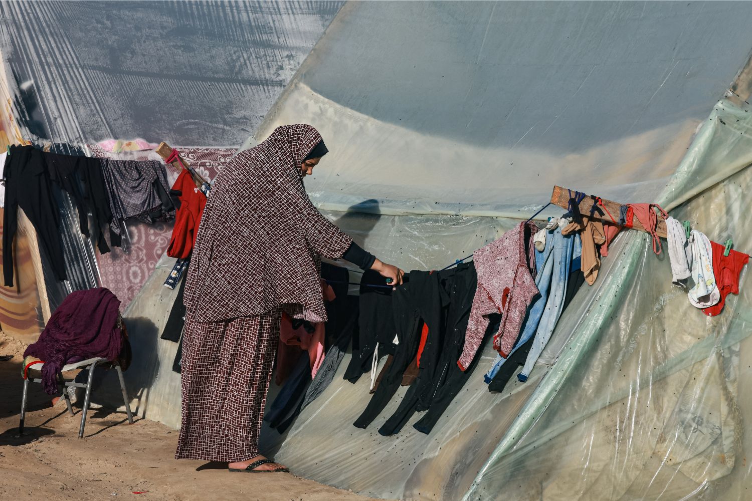 A woman hangs up clothes at a camp for displaced Palestinians in Rafah in the southern Gaza Strip on December 16, 2023, amid continuing battles between Israel and the militant group Hamas. (Photo by MOHAMMED ABED / AFP)