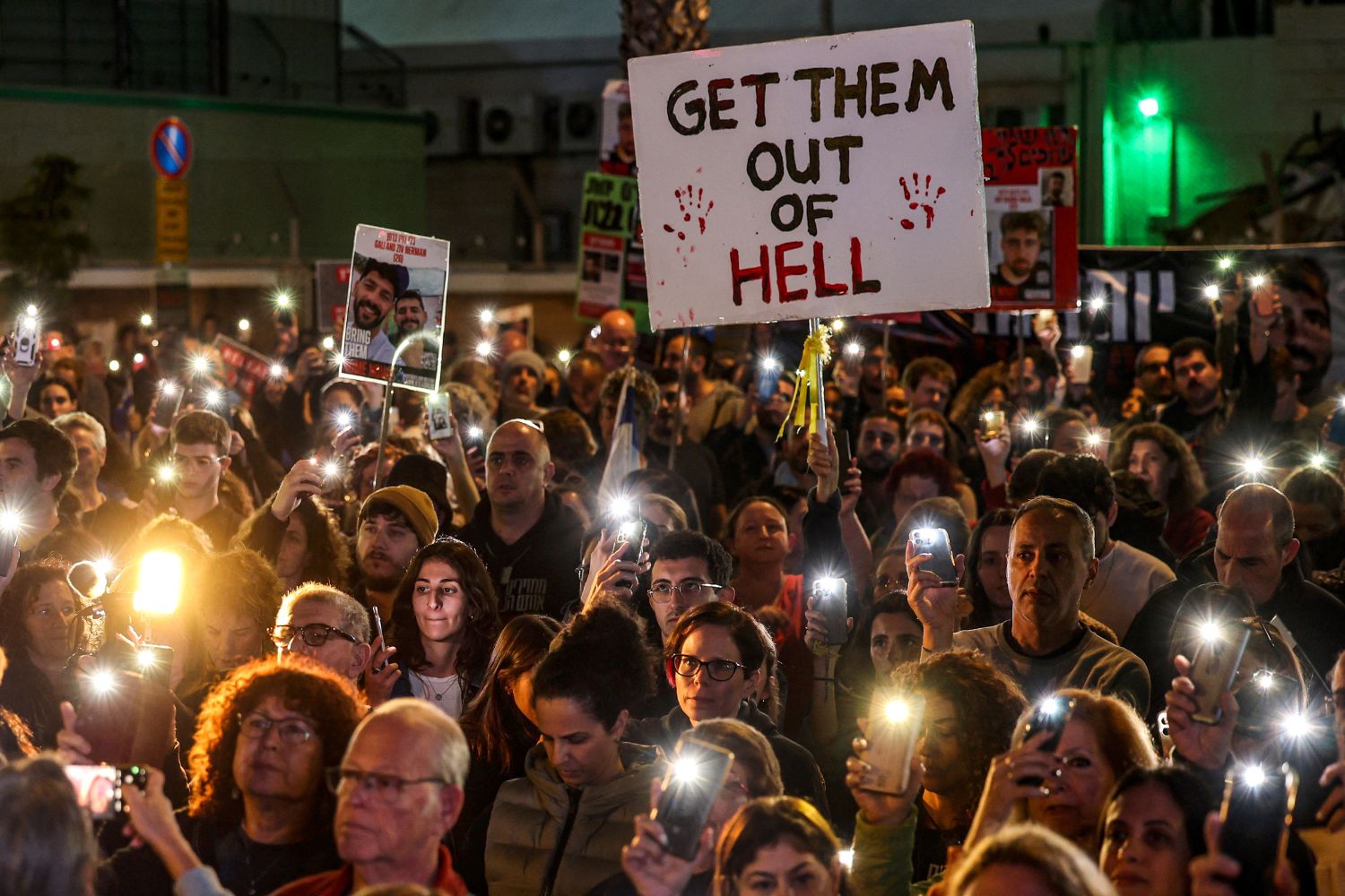 Relatives and supporters light their phones around a placard reading "Get them out of hell" during a rally calling for the release of Israeli hostages held in Gaza since the October 7 attacks by Hamas in southern Israel, in Tel Aviv on December 30, 2023. (Photo by AHMAD GHARABLI / AFP)