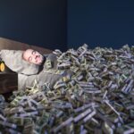 Smiling man sleeping in a bed covered with dollars money. wealth concept.