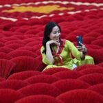 In this photo taken on January 20, 2024 a tourist takes a selfie picture in front of incense sticks arranged in the form of a Vietnamese flag in a courtyard in the village of Quang Phu Cau on the outskirts of Hanoi. Families living and working in the "incense village" of Quang Phu Cau now also make sticks in yellow, blue and green, catering to visitors eager to snap shots for Instagram. (Photo by Nhac NGUYEN / AFP)