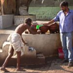 Orchha, Madhya Pradesh, India - May 7 2016: A low caste man (dalit), bending, is served water from a distance. He does not even gets close to the man serving him. Dalit is a name for people who used to belong to the lowest caste in India, previously characterized as "untouchables".